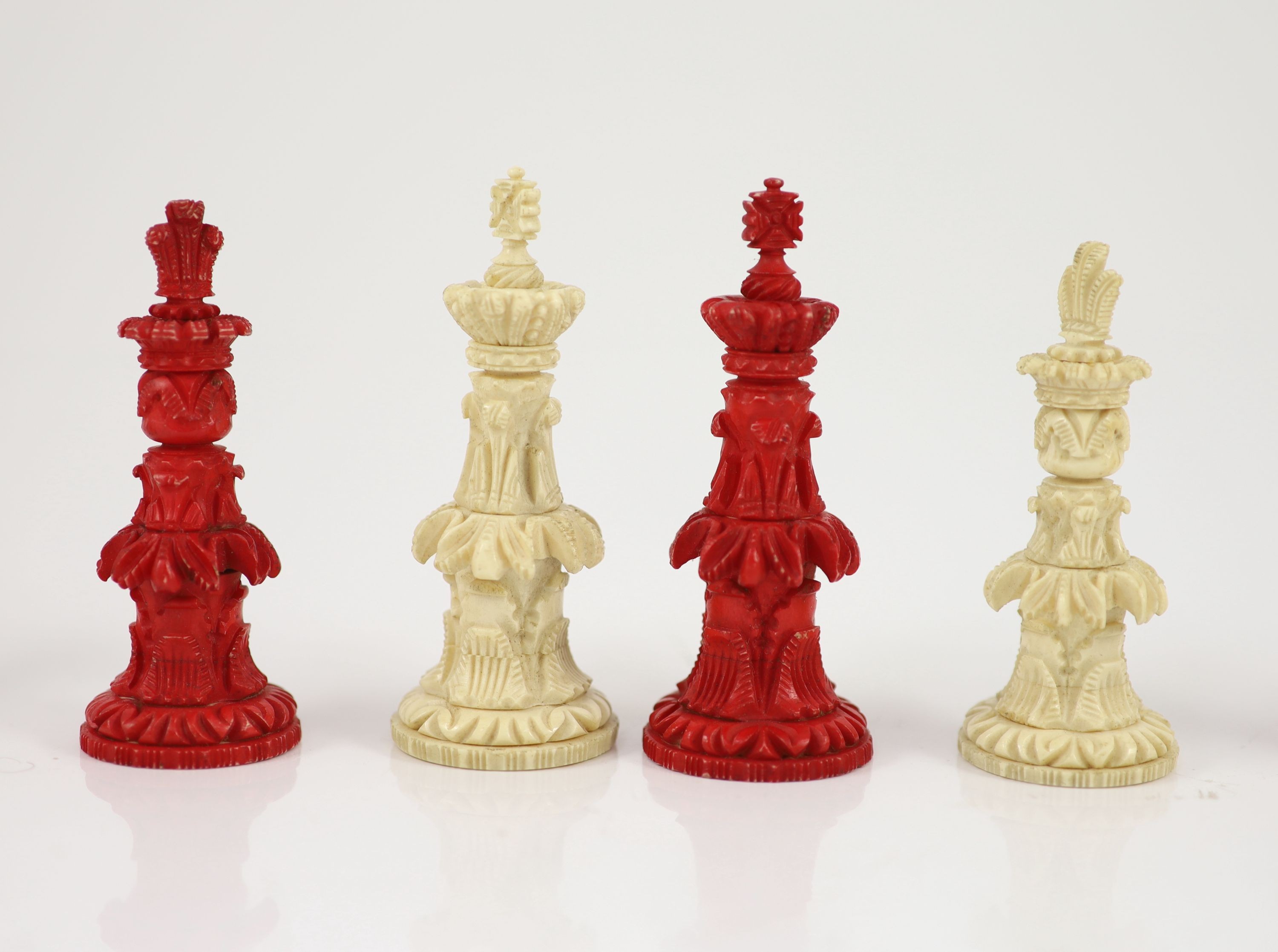 A 19th century Anglo-Indian white and red stained bone chess set, with unusual carved palmate decoration, Kings 9.5cm.